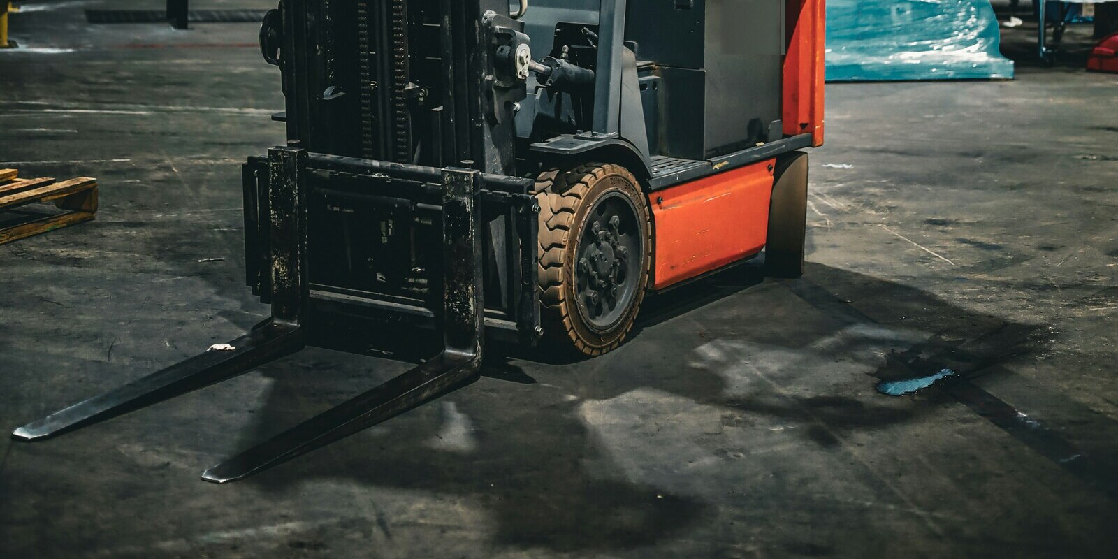 Forklift forks and mast lowered to a warehouse floor beside its drive wheel